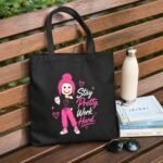 A lifestyle view of the 'Stay Pretty Work Hard' black canvas tote bag by Stilotee. Featuring an empowering quote and a stylish pink graphic, this durable aesthetic tote bag is a perfect daily companion for the modern, hard-working woman.