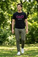 Man standing outdoors in a park wearing a black cotton t-shirt featuring the iconic Squid Game circle, triangle, and square symbols