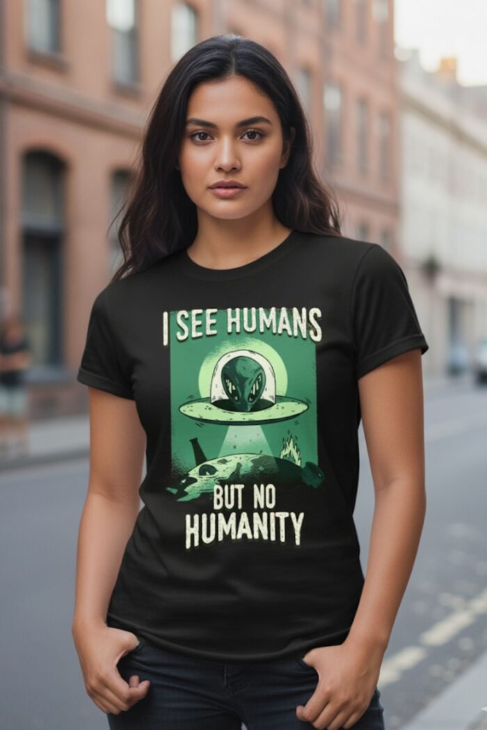 Woman standing outdoors wearing a black cotton t-shirt featuring a green alien graphic and the quote I See Humans But No Humanity