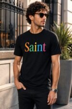 Male model wearing the Saint black t-shirt with rainbow typography graphic – premium cotton unisex streetwear lifestyle shot