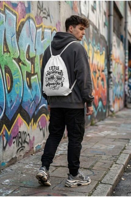 Back view of a model wearing Stilotee white canvas drawstring backpack with minimalist typography print against a colorful urban graffiti wall