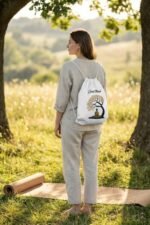 Model from behind wearing the Stilotee white canvas drawstring backpack with Zen Buddha design near an urban concrete wall