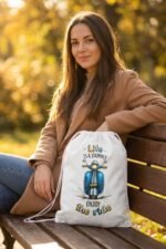 Model wearing a brown jacket showcasing the Stilotee white canvas drawstring backpack with vintage blue scooter graphic