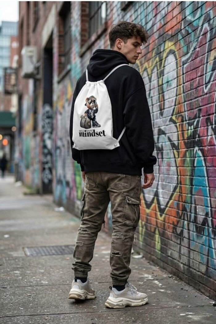 Back view of a person wearing a black hoodie and Stilotee white canvas gym sackpack walking near a graffiti wall