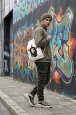 A female model walking down a city street wearing a white canvas drawstring bag with a red and black Che Guevara graphic print.