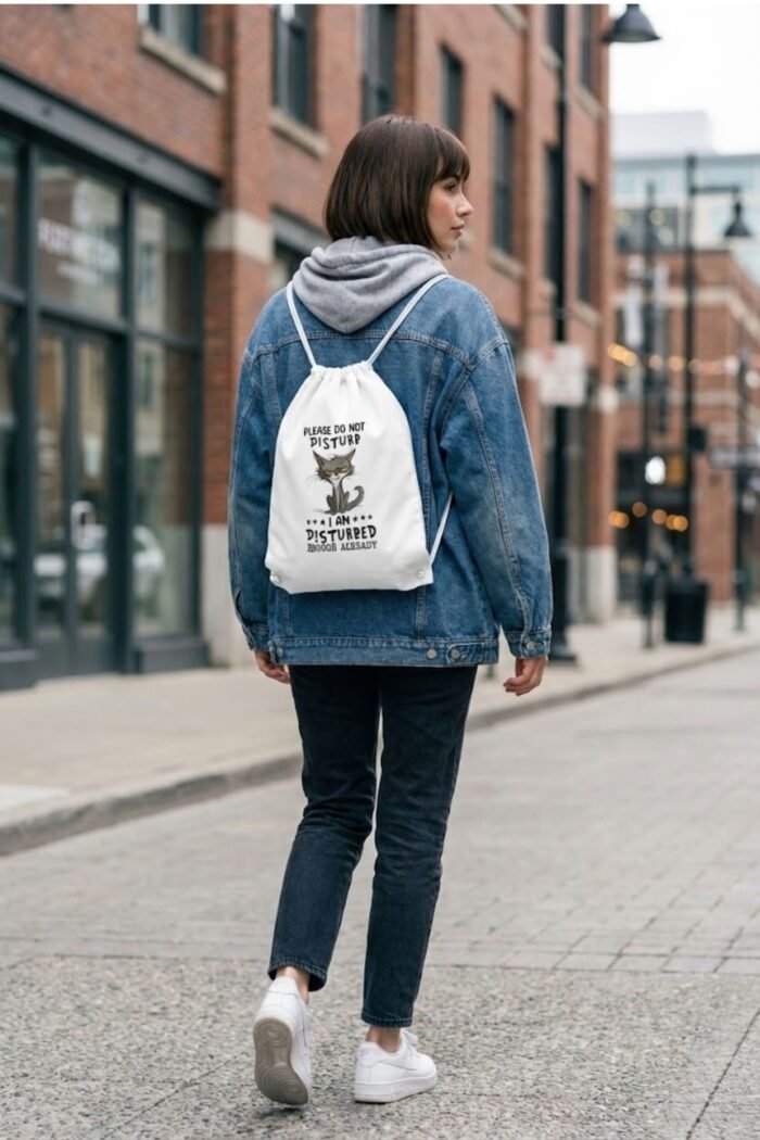 A person wearing a white canvas drawstring bag with a sarcastic cat meme graphic walking down an urban street.