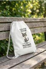 The white introvert sarcastic cat drawstring gym bag displayed flat on a textured surface next to a grey rolled-up yoga mat.