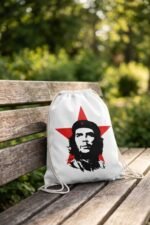 The Che Guevara graphic drawstring bag displayed flat on a white wooden surface next to vintage glasses and a camera.