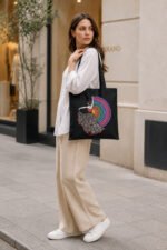 Woman carrying black canvas tote bag with vibrant folk art dance print over shoulder for daily shopping and college commute