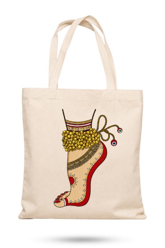 Off-white canvas tote bag featuring an Indian classical dancer foot adorned with golden ghungroo bells, red alta dye, and ornamental anklet with zipper closure.