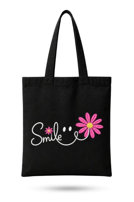 Black heavyweight canvas tote bag featuring white cursive Smile text with pink daisy flowers and smiley face graphic with zipper closure.